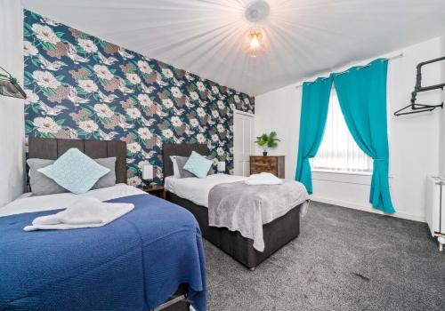 Duas camas num quarto com cortinas azuis e papel de parede floral em Lady Wilson Apartment by Klass Living Airdrie em Airdrie