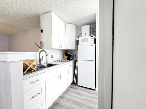 a white kitchen with a sink and a refrigerator at Purple Reign: A Chic, Romantic Oceanfront Getaway - Sleeps 4 in Daytona Beach