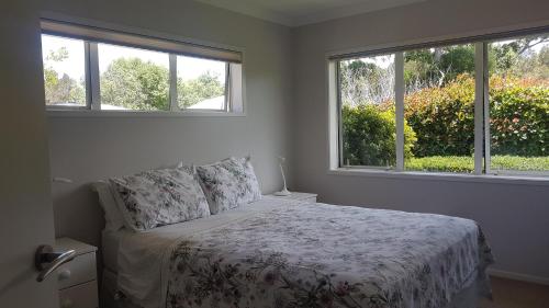 a white bedroom with a bed and two windows at Mangawhai Heads apartment in Mangawhai
