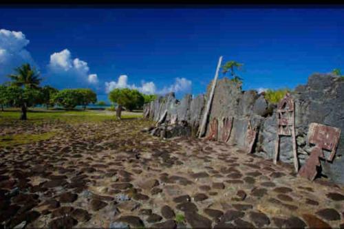 a stone wall with a fence in a field at Bungalow climatisé chez Kim in Taputapuapea