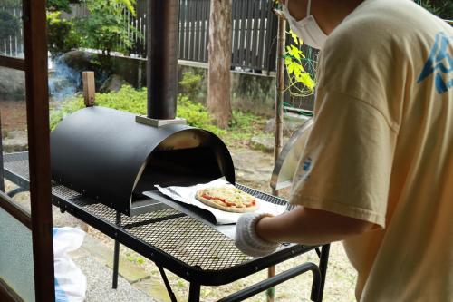 a man cooking a pizza in an outdoor grill at Abuden in Kumano for women and families 女性と家族専用の宿 in Kumano