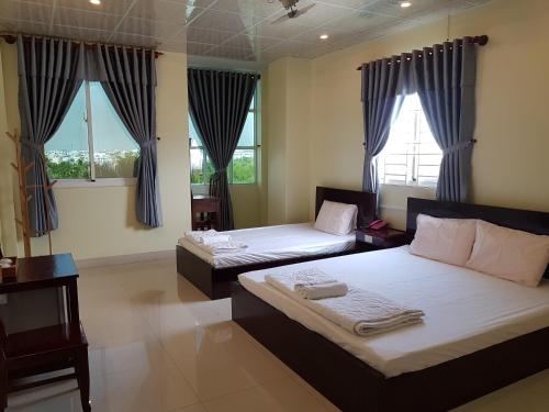 a bedroom with two beds and two windows at Hostel Đặng Lợi ホステルダンロイ in Chau Doc