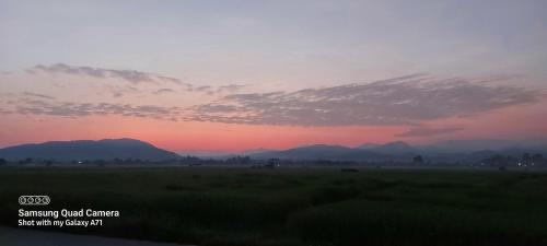 een zonsondergang boven een veld met bergen op de achtergrond bij บ้านพิงค์นา in Mae Tha
