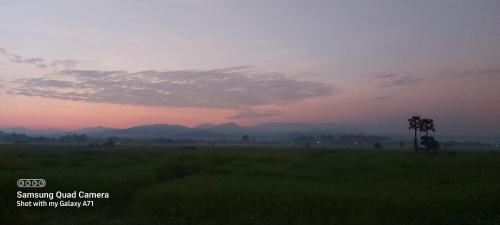een zonsondergang in een veld met bergen op de achtergrond bij บ้านพิงค์นา in Mae Tha