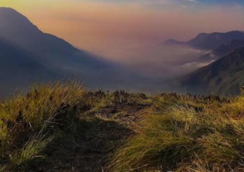 a view of a mountain with clouds in the sky at Munnar green portico cottage in Munnar