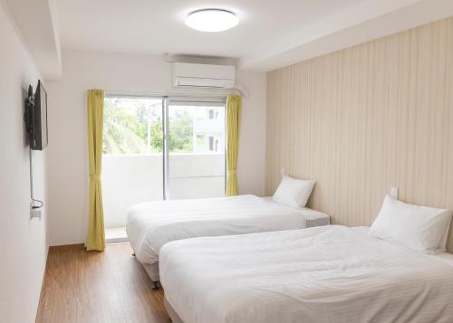 two beds in a room with a window at BiBi Hotel 宮古空港前 in Miyako-jima