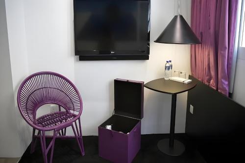 um quarto com uma cadeira roxa, uma mesa e uma televisão em Hi Hotel Bugis em Singapura