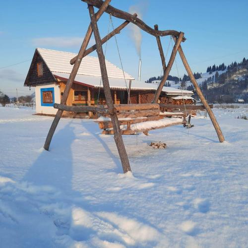 a wooden swing in the snow in front of a house at Casa Bunicii in Topliţa