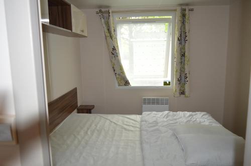 um quarto com uma cama branca e uma janela em mobil home em Sainte-Reine-de-Bretagne
