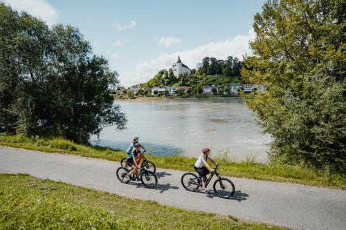 3 Leute fahren Fahrrad auf einem Weg neben einem Fluss in der Unterkunft Privatzimmer - Sieben an der Donau in Ottensheim
