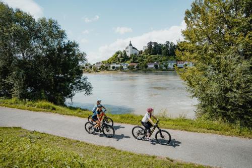 three people riding bikes down a path next to a river at Privatzimmer - Sieben an der Donau in Ottensheim