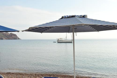 a blue and white umbrella on a beach with a boat at Beachfront Lampis Dolphin 1 in Skala