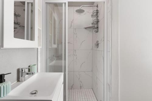baño blanco con ducha y lavamanos en Nirvana 12 en Bloubergstrand