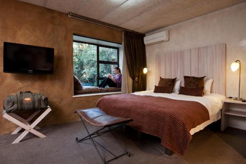 una habitación de hotel con una cama y una persona sentada en una ventana en African Rock Hotel and Spa, en Kempton Park