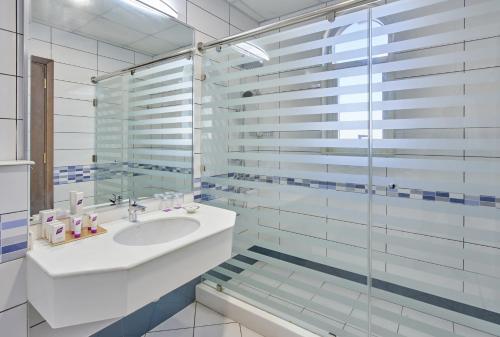 uma casa de banho com um lavatório e uma cabina de duche em vidro. em TIME Express Hotel Al Khan em Sharjah