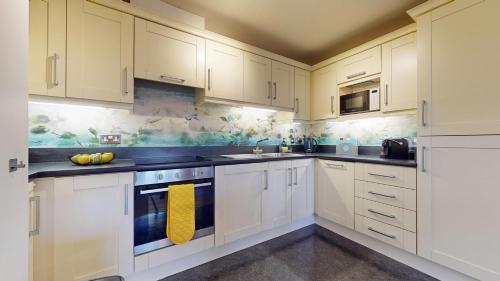 Una cocina blanca con armarios blancos y una toalla amarilla. en Stylish Central Apartment en Beckenham