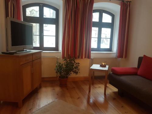 a living room with a tv and a couch and two windows at Ferienwohnung an der Nikolaikirche in Görlitz