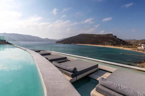 a swimming pool with chaise lounges next to the ocean at Panormos Village Hotel in Panormos Mykonos
