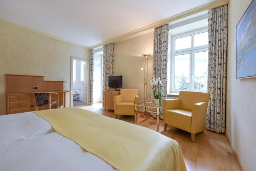 a bedroom with a bed and two chairs and a television at Cresta Palace Celerina in Celerina