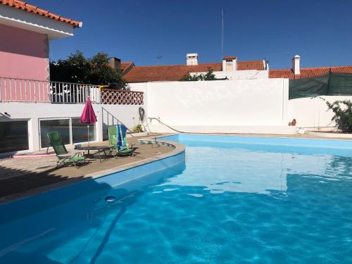 a swimming pool with two chairs and an umbrella at CASA ROSA COSY PINK GUEST HOUSE in Torrão