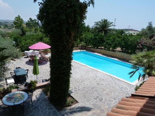 a pool with a tree next to a table and umbrella at Poggio Delle Palme in Campobello di Licata