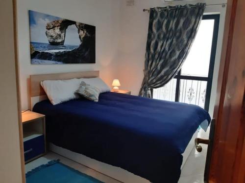 a bedroom with a blue bed and a window at Xlendi Home in Xlendi