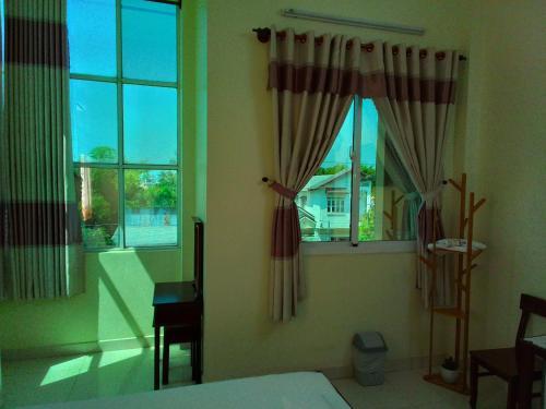 a bedroom with a bed and two windows and a desk at Hostel Đặng Lợi ホステルダンロイ in Chau Doc