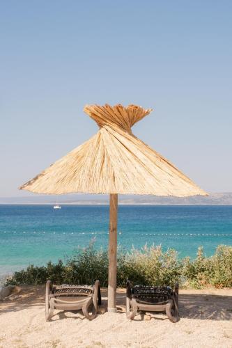 a straw umbrella on the beach with two benches at PAVI APARTMENTS Life Style House with private pool in Kornić