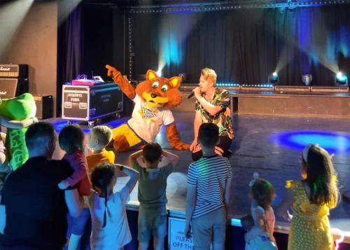 a group of children watching a woman in a tiger mascot on a stage at Stanwix Park in Silloth