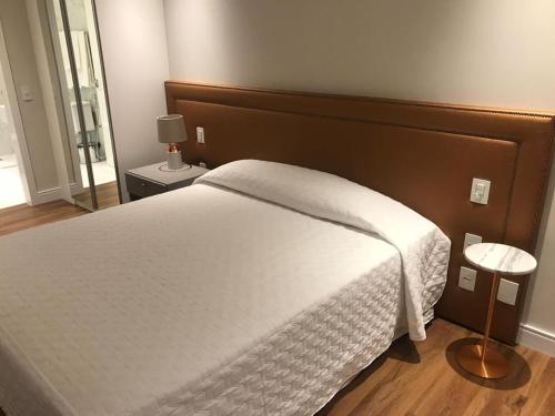 um quarto com uma cama branca e uma cabeceira em madeira em Estúdio novo com serviço de hotel em Florianópolis