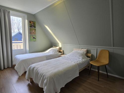 a bedroom with two beds and a chair and a window at Natuurvilla De Heerlickheyt in Hoogersmilde