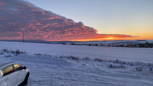 a car parked in a snow covered field with the sunset at Chalet Sijkovsky in Stará Lesná