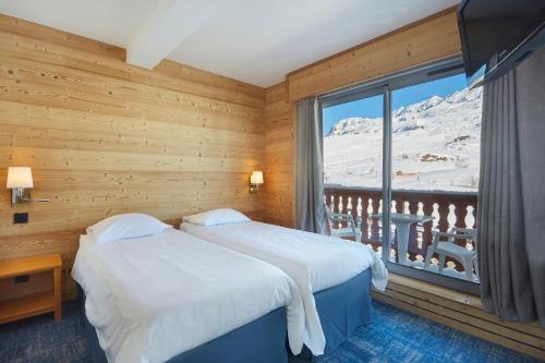 een slaapkamer met 2 bedden en een raam met besneeuwde bergen bij Hôtel Eliova Le Chaix in L'Alpe-d'Huez