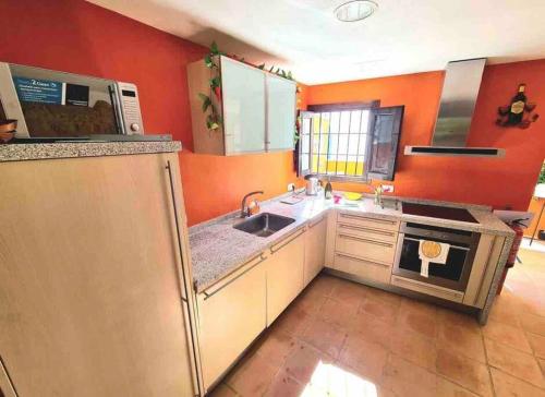 cocina con paredes de color naranja, fregadero y fogones en La Casa Siglo Ocho, en Iznájar