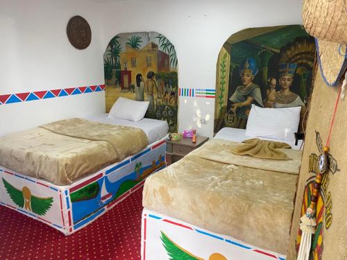 peace garden hostel & camp في الأقصر: سريرين في غرفة بها لوحات على الجدران