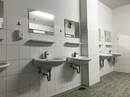 uma casa de banho pública com três lavatórios e espelhos em EuroCup Campsite 2024 em Munique