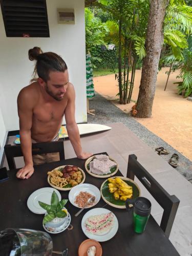 a shirtless man sitting at a table with food on it at AURORA Midigama in Ahangama
