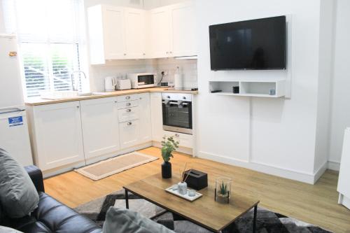een keuken met witte kasten en een tafel en een tv bij Cosy house in West Yorkshire in Batley