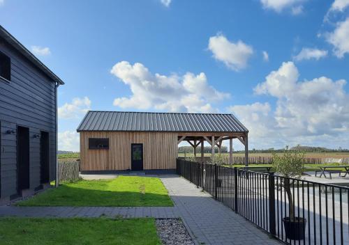 a wooden building with a metal roof next to a fence at Bramendijk in Groede
