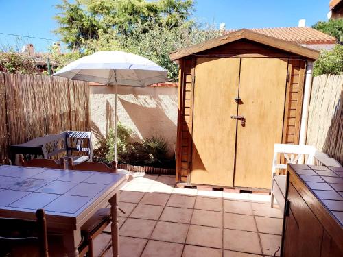 un hangar en bois avec une table et un parasol dans l'établissement Maison 10min à pied de la plage, à Saint-Cyprien