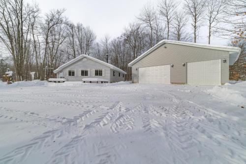 a house with a lot of snow in front of a garage at Secluded Mancelona Home with Gas Grill! in Mancelona