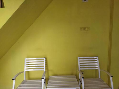 2 chaises blanches assises à côté d'un mur jaune dans l'établissement OYO 93306 Penginapan Permata Hijau Syariah, à Parepare