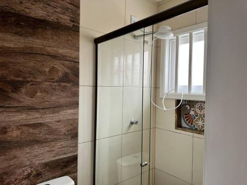 La salle de bains est pourvue d'une douche en verre avec un mur en bois. dans l'établissement Belíssima casa a perto da praia, à Tramandaí