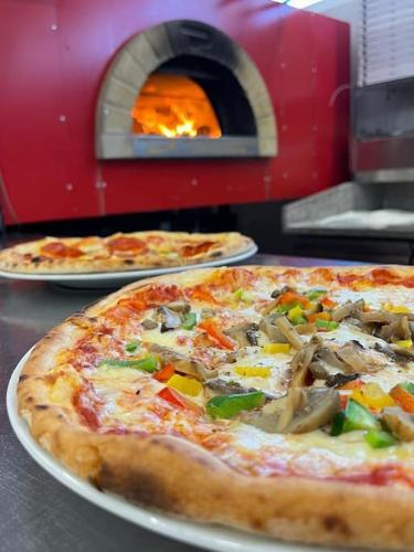 two pizzas on plates on a table with a pizza oven at Villa Miri Rosemary in Privlaka