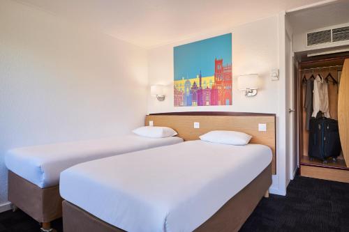 two beds in a hotel room with a painting on the wall at Kyriad Direct Haguenau in Haguenau