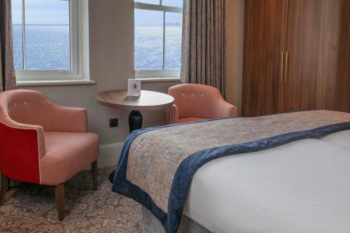 a hotel room with a bed and a chair and window at voco The Clifton Folkestone by IHG in Folkestone