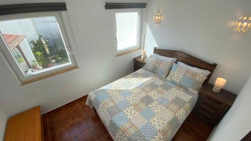 a bedroom with a bed with a quilt and two windows at Apartamento Miradouro in Carrapateira