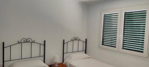 a white bedroom with two beds and a window at ATICOS Primera Linea en ZAHARA DE LOS ATUNES in Zahara de los Atunes