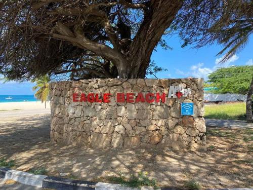 a stone wall with a sign that reads eagle beach at Beautiful Vibes Sun Kiss Serenity your Stylish Apt Just Steps from Eagle Beach in Palm-Eagle Beach
