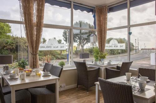 un restaurante con mesas, sillas y ventanas grandes en The New England, en Eastbourne